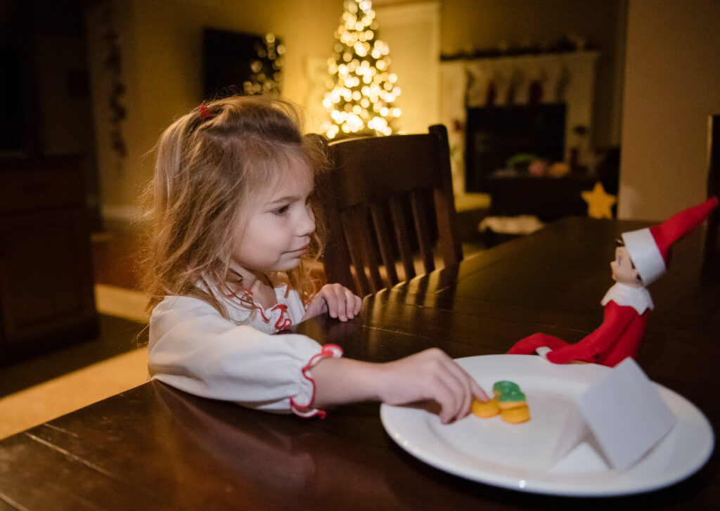 little girl looking at her elf on the shelf and donuts