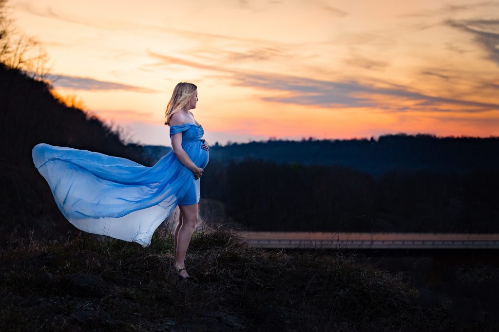 pregnant mother with flow blue sew trendy dress at mountain top with sunset 