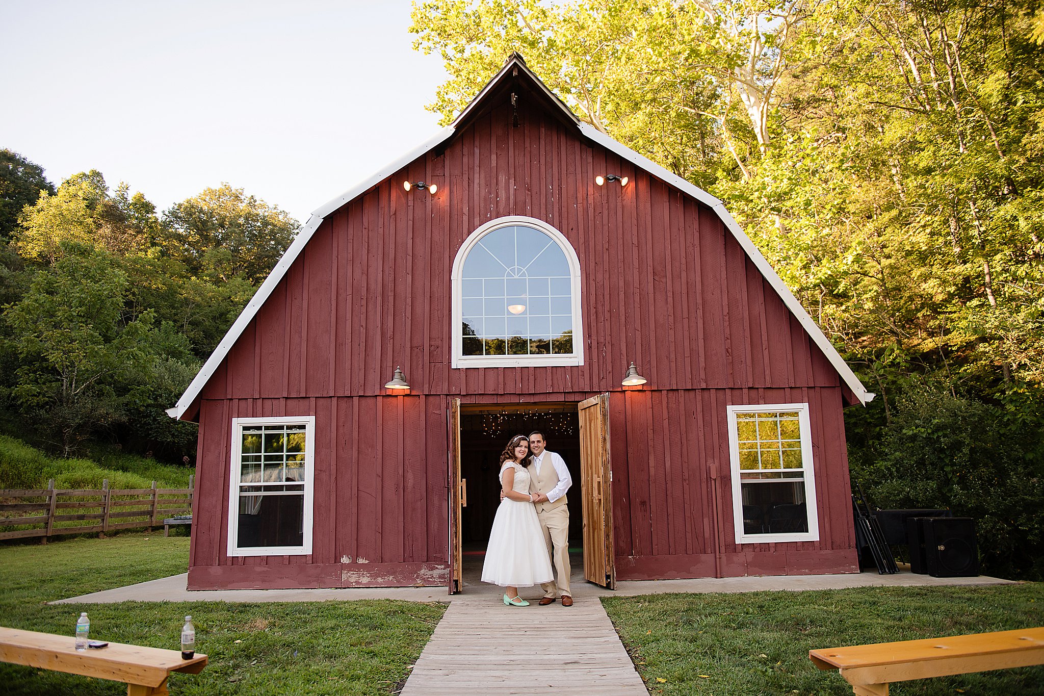 wedding couple stand together in front of red a-frame barn at Ransom Hollows venue in Ripley wv