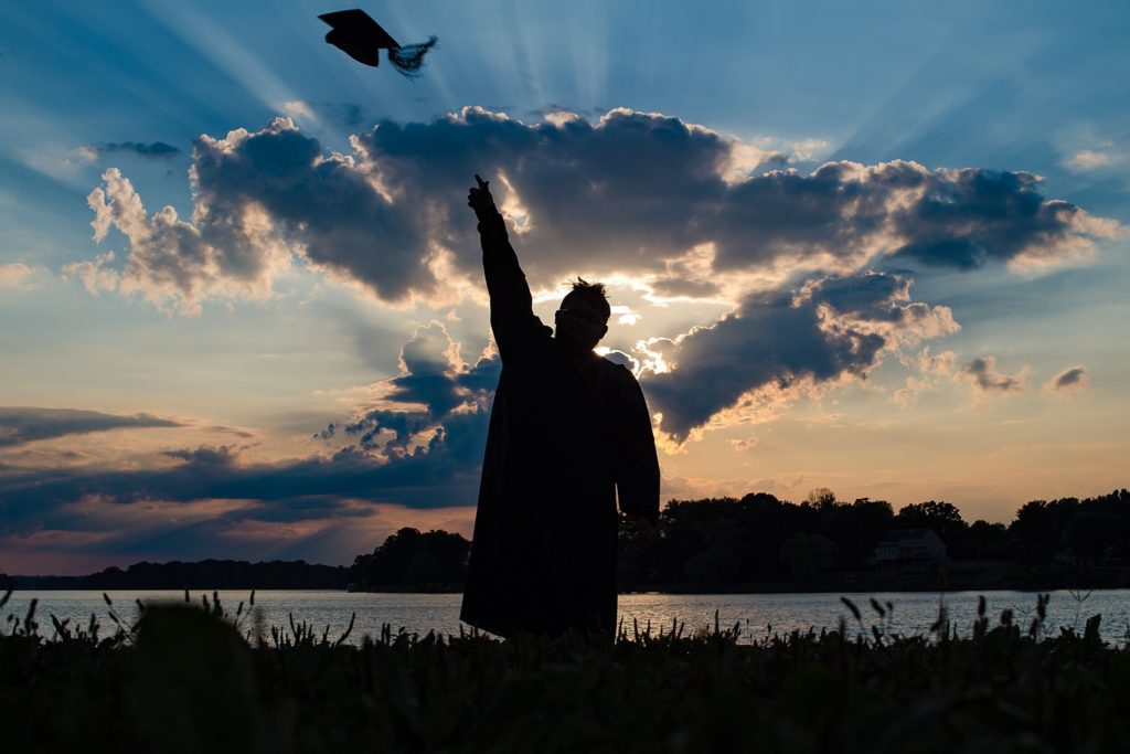 Silhouette of a boy throwing his cap from his cap and gown session