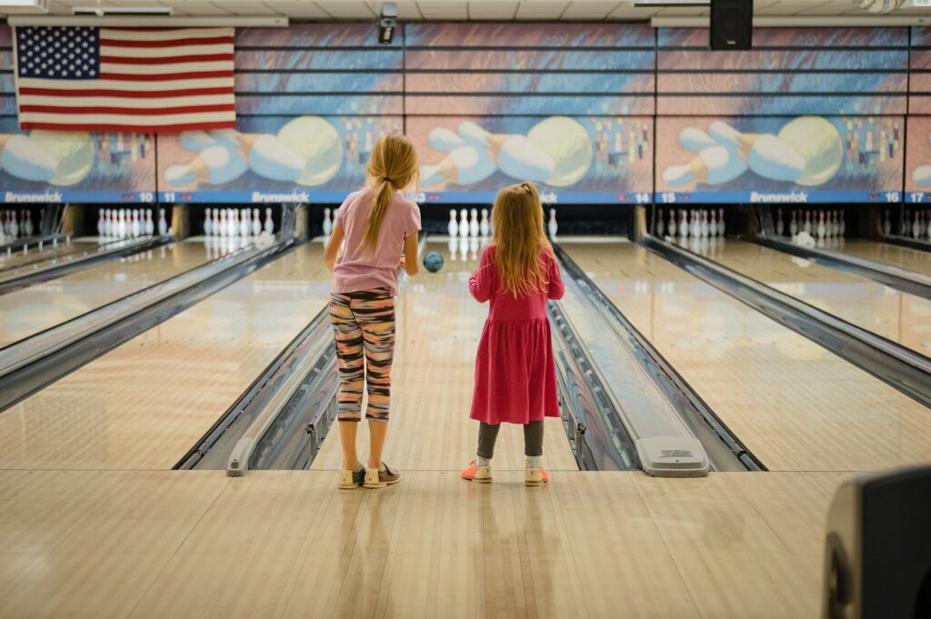two little girls watch ball roll down lane at emerson bowling lanes