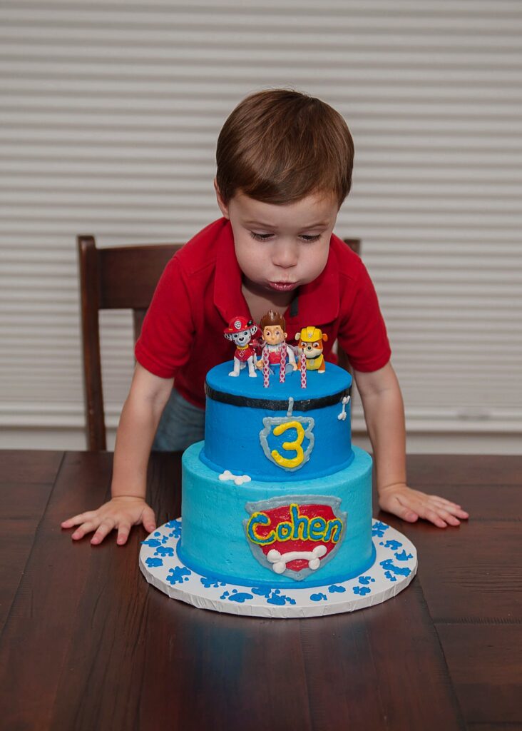little boy blowing out birthday candles on blue two layer birthday cake