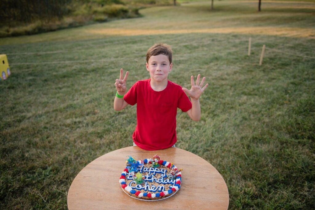 birthday boy holding up fingers by sky landers cookie cake
