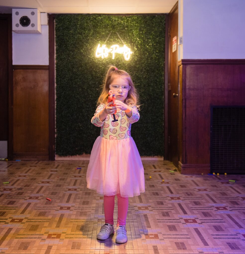 little girl in pink dress aims a nerf gun at birthday party 