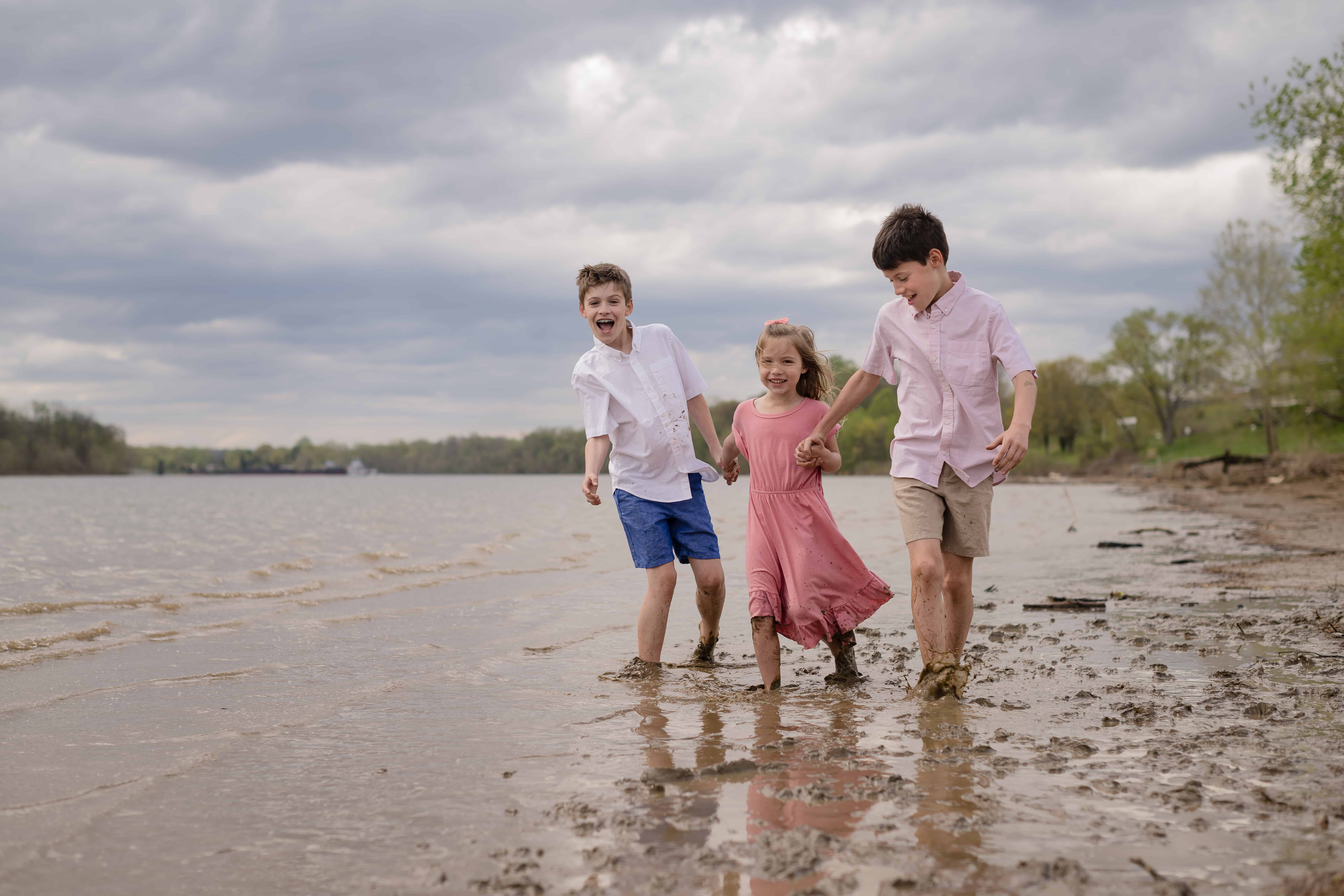 A girl and two boys bonding and having fun at the muddy lake while their hands are intertwined.