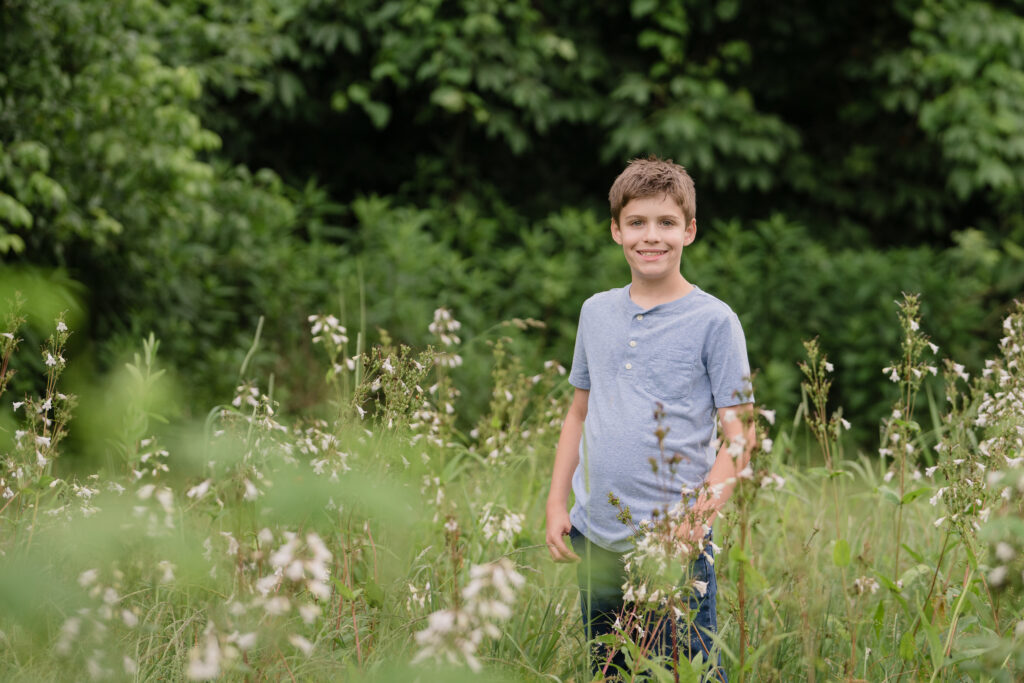 Boy smiling with a flower field behind him. Boy posing in a field for a photography session near Marietta, OH. Lori Pickens Photography took the picture and is based out of Parkersburg, WV