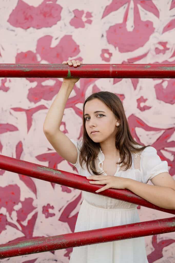 Girl posing in fron tof a vibrant floral red backdrop with her hand on a red railing for her senior session near marietta oh