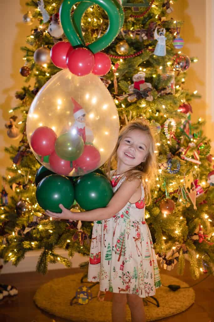 Elf on the Shelf arriving in a balloon ornament with a little girl in front of a christmas tree