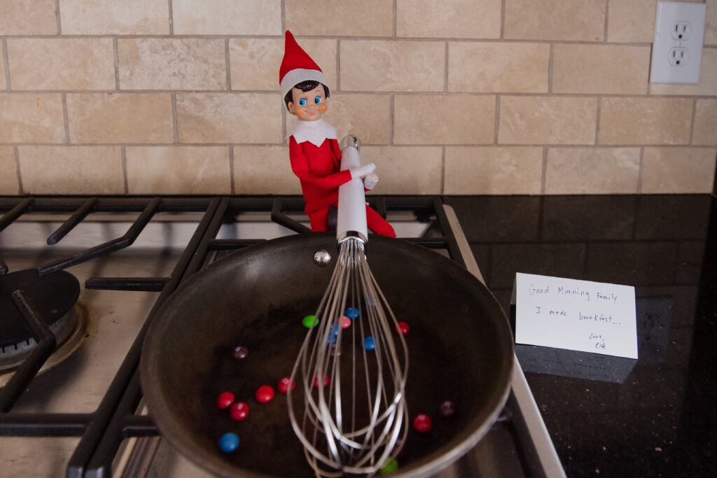 Elf on the shelf cooking skittles in a skillet with a whisk