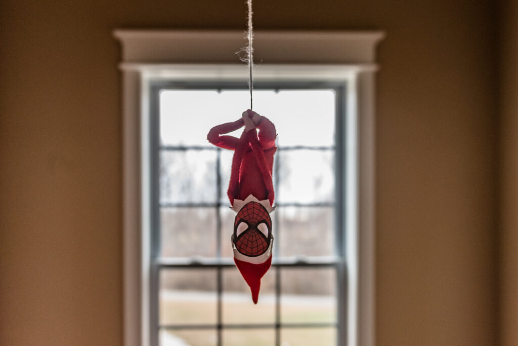 Elf on the Shelf hanging from light fixture as Spiderman