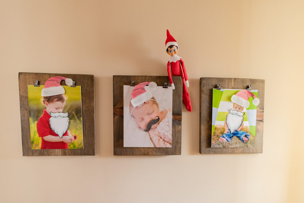 elf on the shelf sitting on a frame.  He has put mustaches and santa hats on the family pictures.