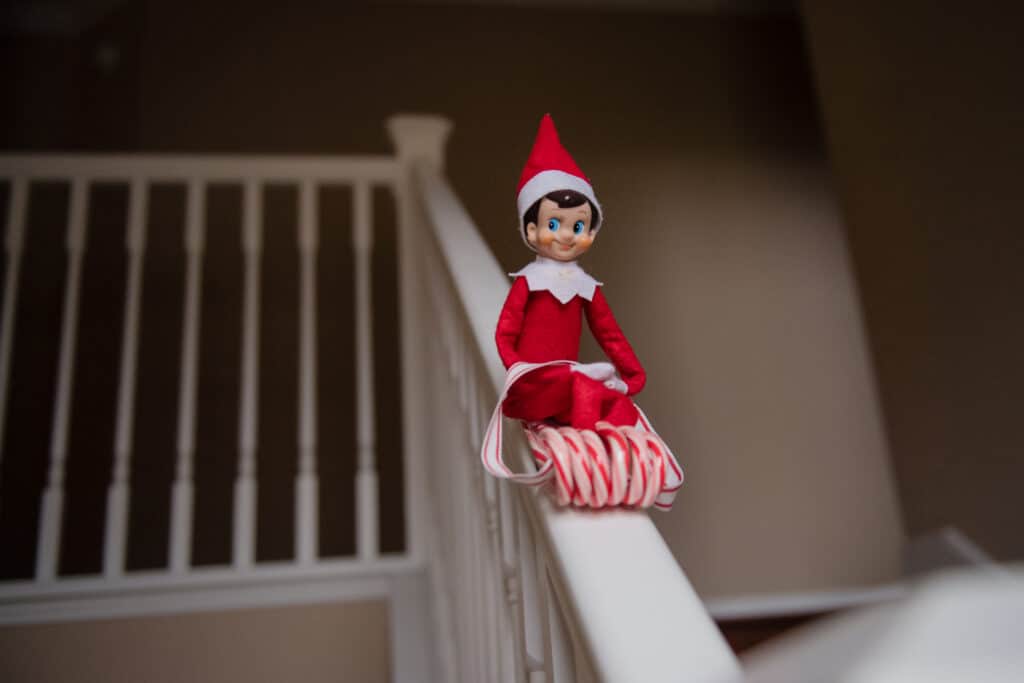 Elf on the Shelf sliding down stair railing on candy cane sled