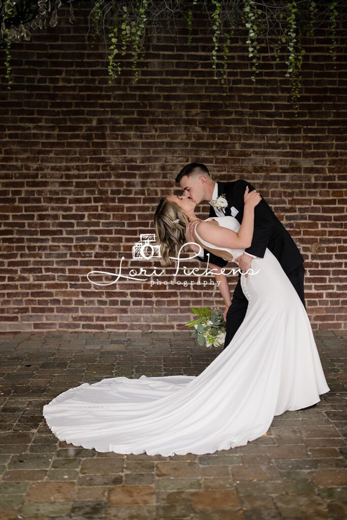 NEwlyweds dip and kiss in front of a brick wall