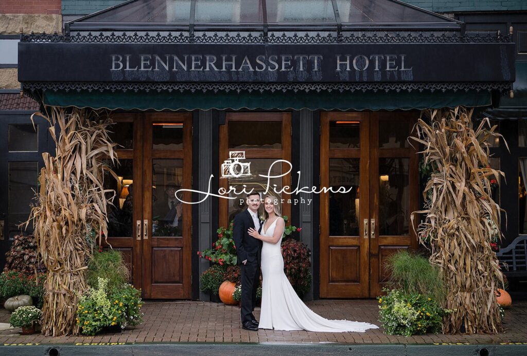 Newlyweds smile while standing under the front facade of their hotel wedding venue