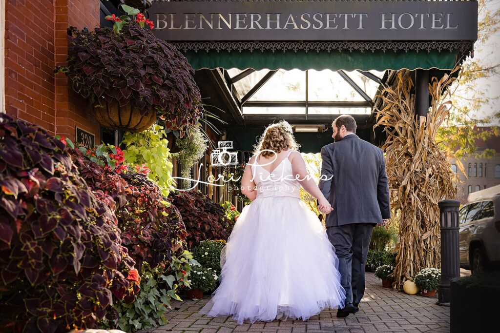 Newlyweds hold hands while walking under the front entrance of the Blennerhassett Hotel wedding venue