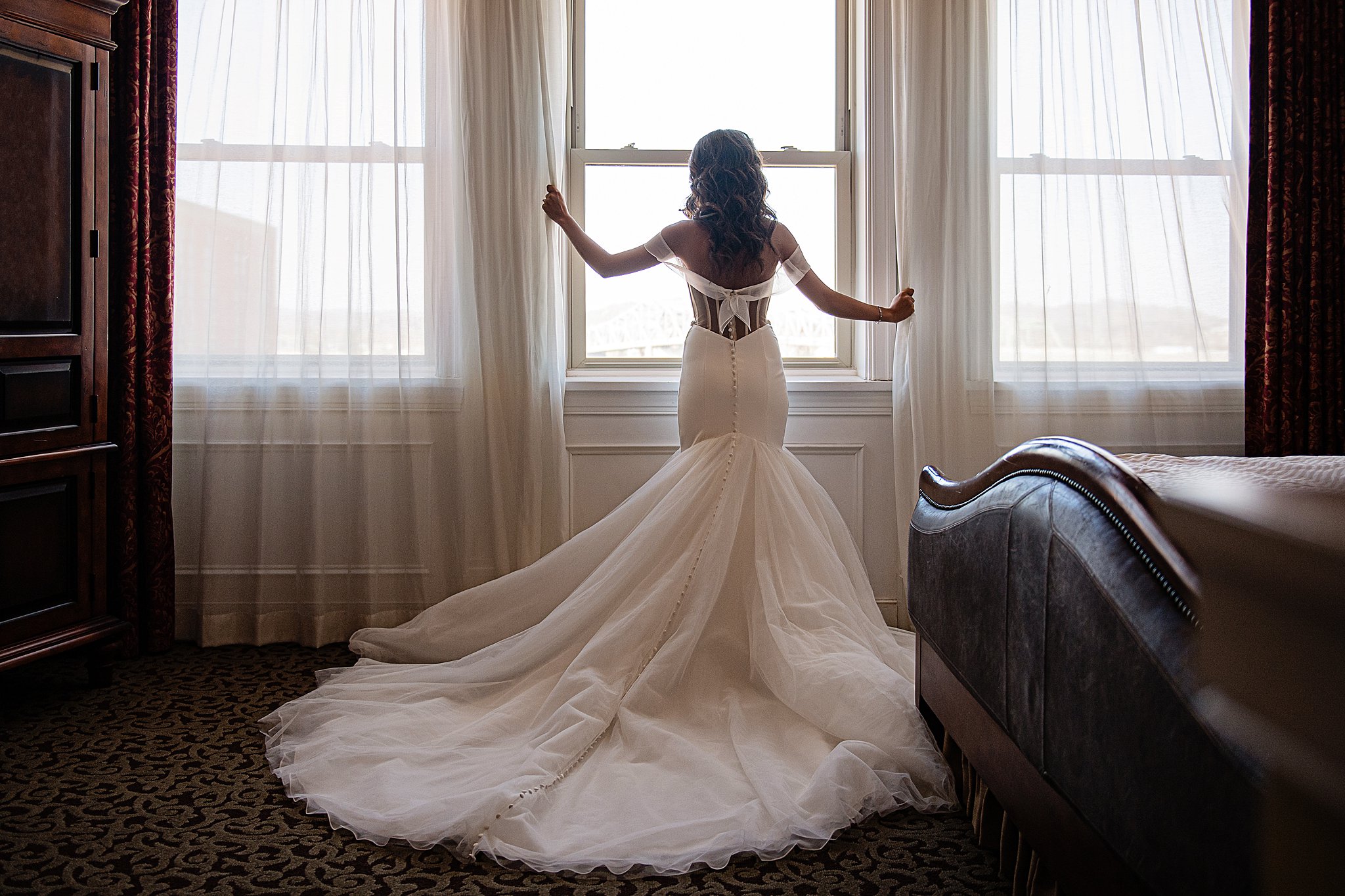 A bride with a long train stands in a window looking out at one of the best wedding venues in parkersburg wv