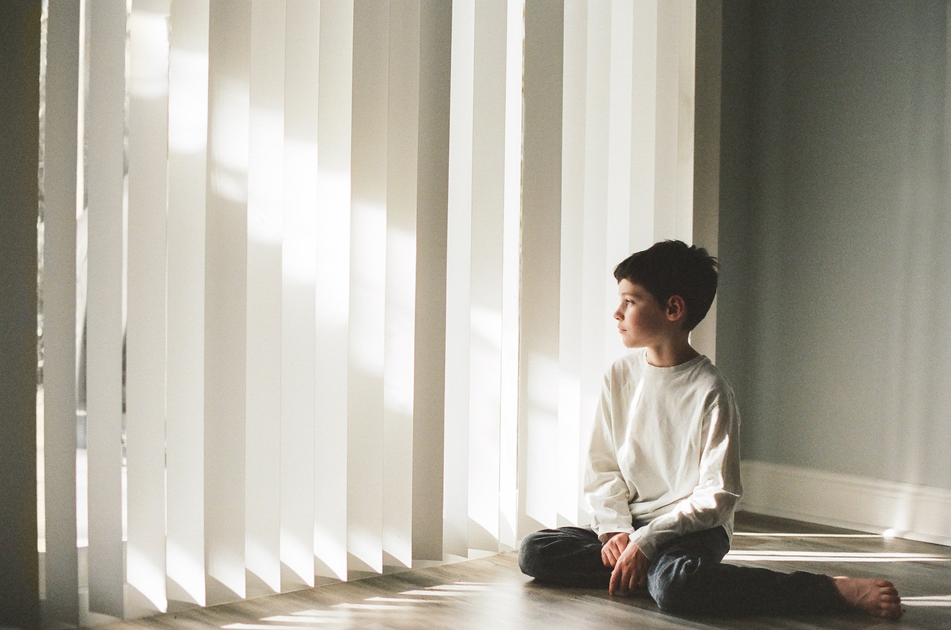 A young boy is engrossed in an activity as he sits on the floor in front of the blinds.
