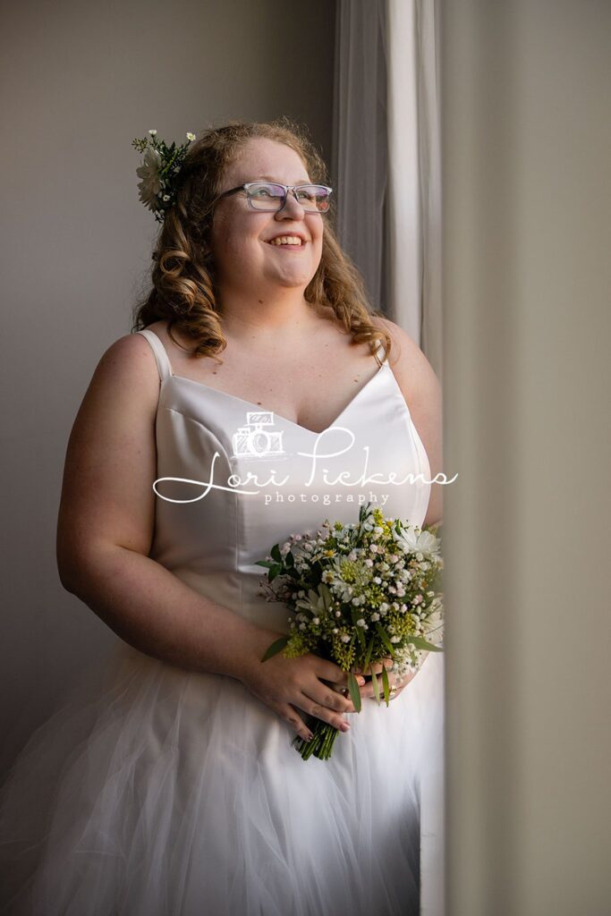 A bride stands in a window holding her bouquet smiling