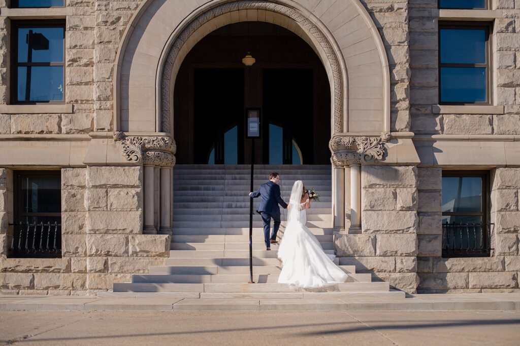 Newlyweds walk up the stone steps of an ornate entrance to a stone building