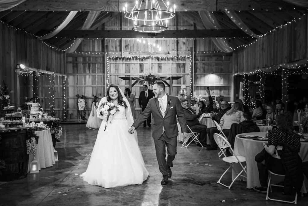 happy wedding couple holding hands and smiling after saying I do in the Barn at Willow Creek in Davisville, WV photo shown with twinkle lights processed in black and white 