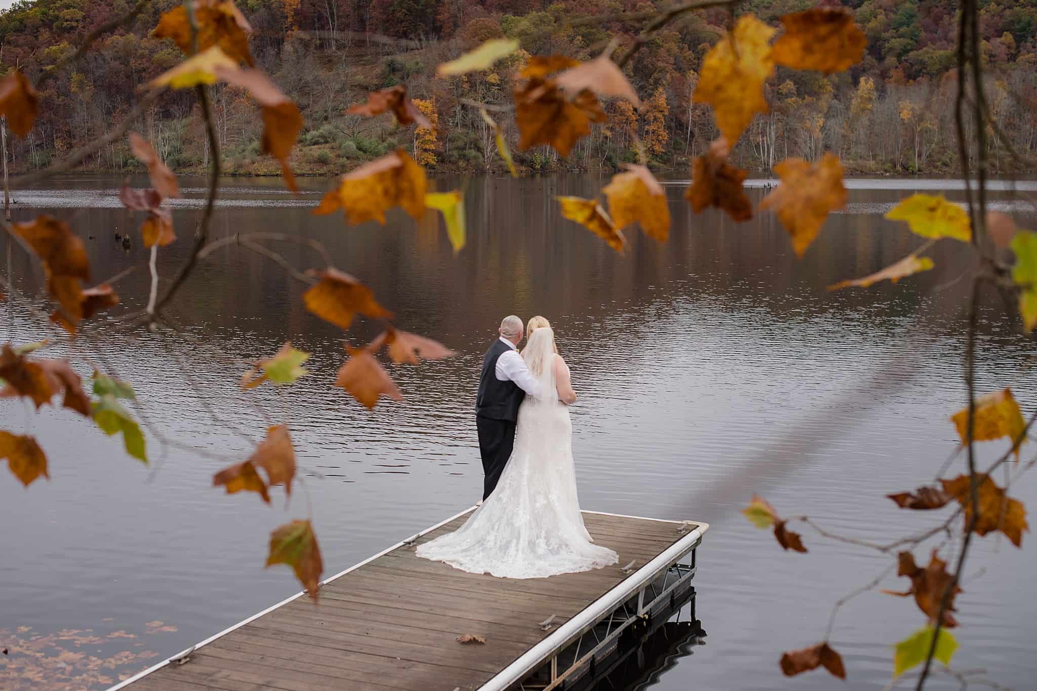 bridal couple standing on a boat dock with water in front of them with fall leaves framing them in WV