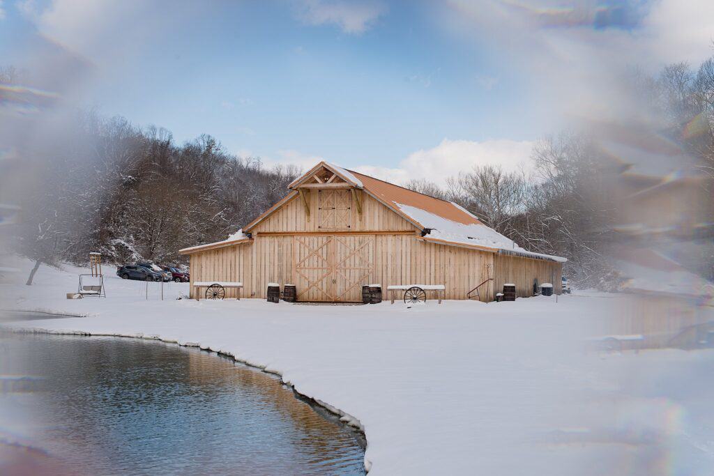 Snow cover barn wedding venue with pond in front and prism effect on the edges called the Barn at Willow Creek in Davisville WV
