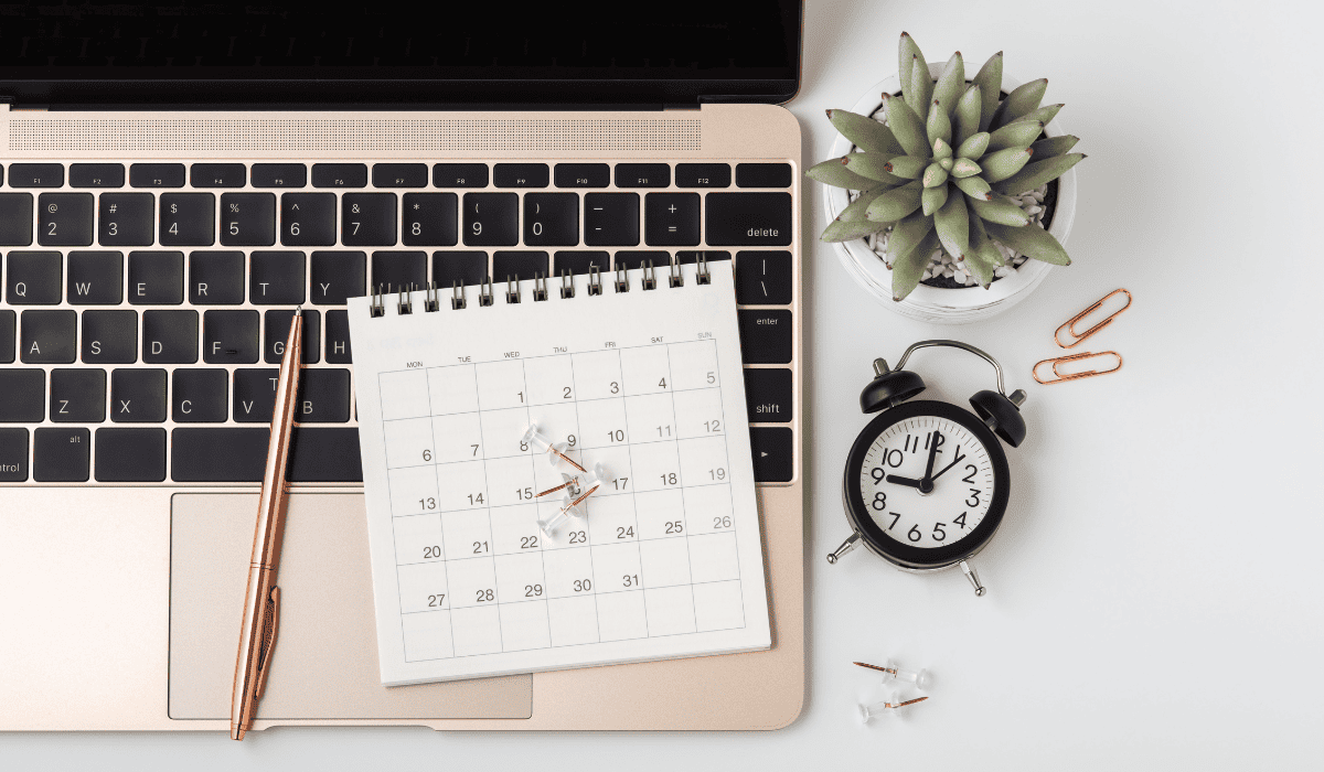 laptop on a desk with a calendar, clock, and succulent.