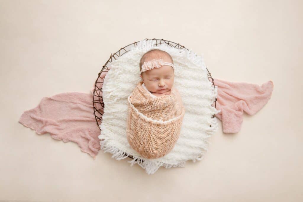 baby swaddled in a basket with a pink shawl begin it