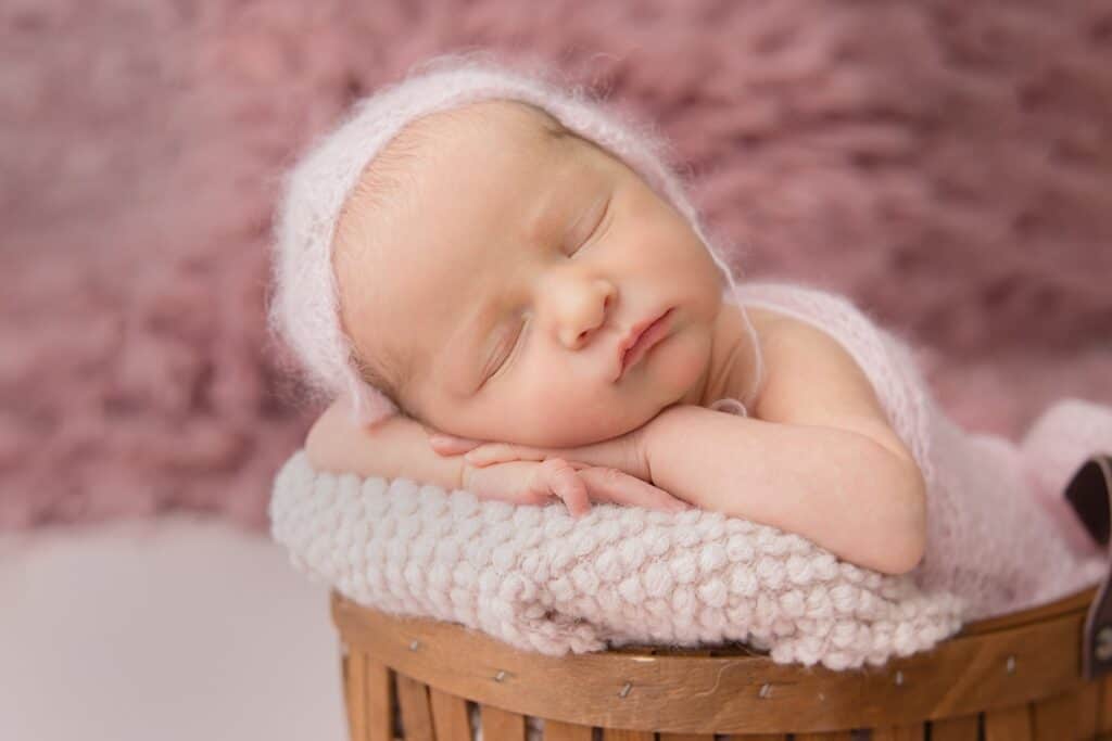 Baby swaddled in a pink knit outfit in a basket with its arms curled under its head