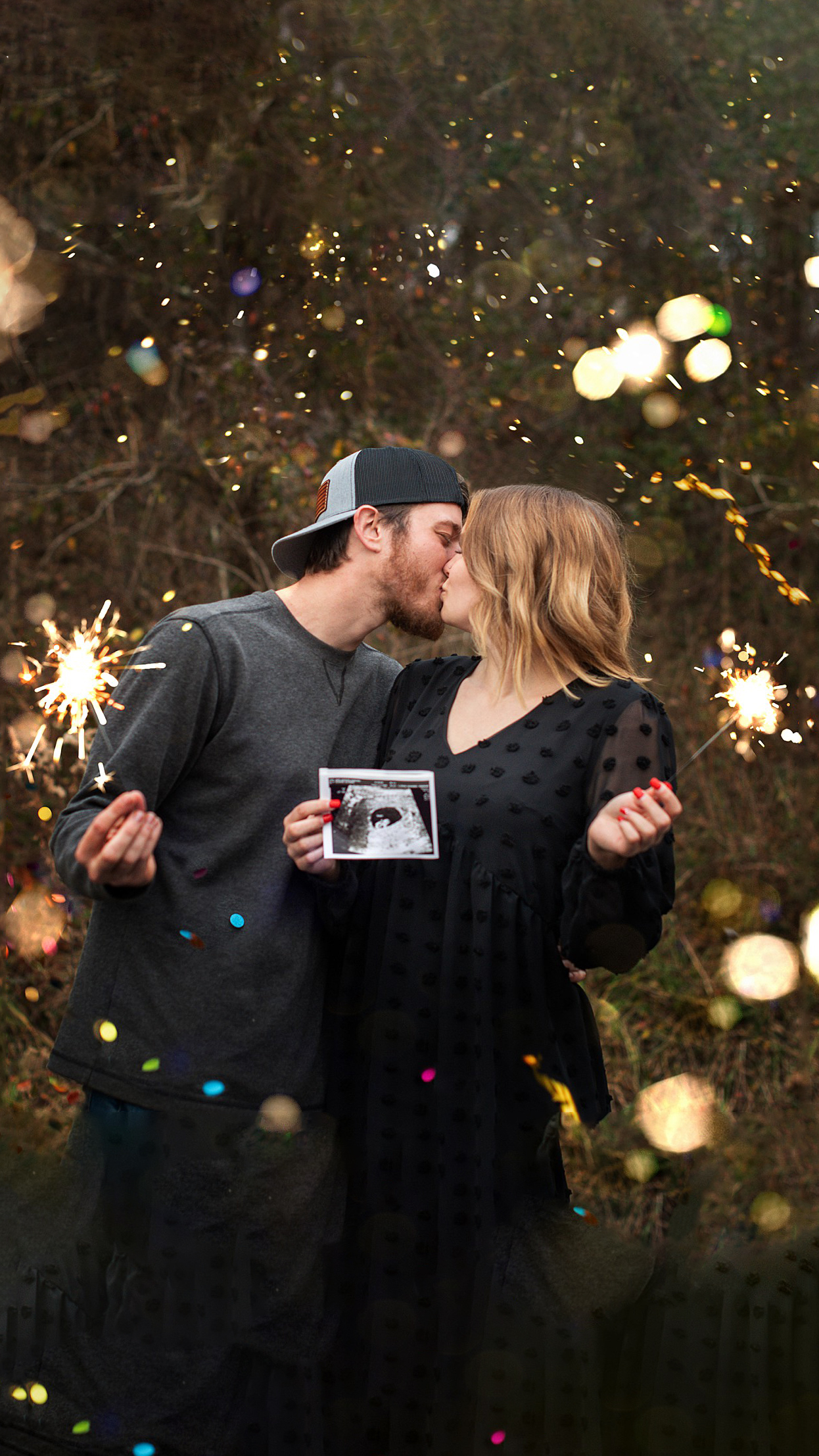 An expecting couple kiss while holding spaklers in black outfits and holding a sonogram after a 4d ultrasound in athens ohio