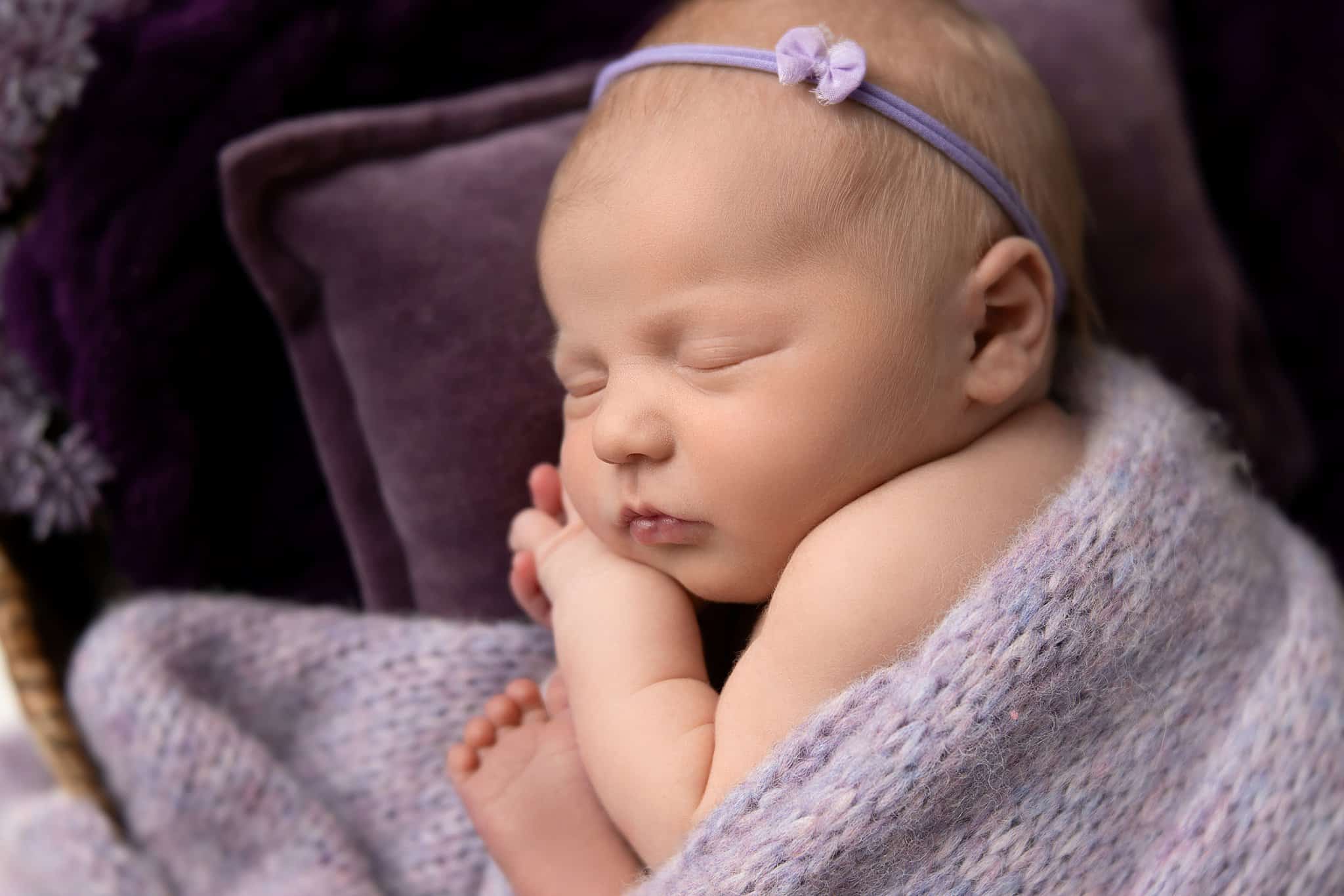 A newborn baby sleeps under a purple knit blanket before visiting parker's playhouse