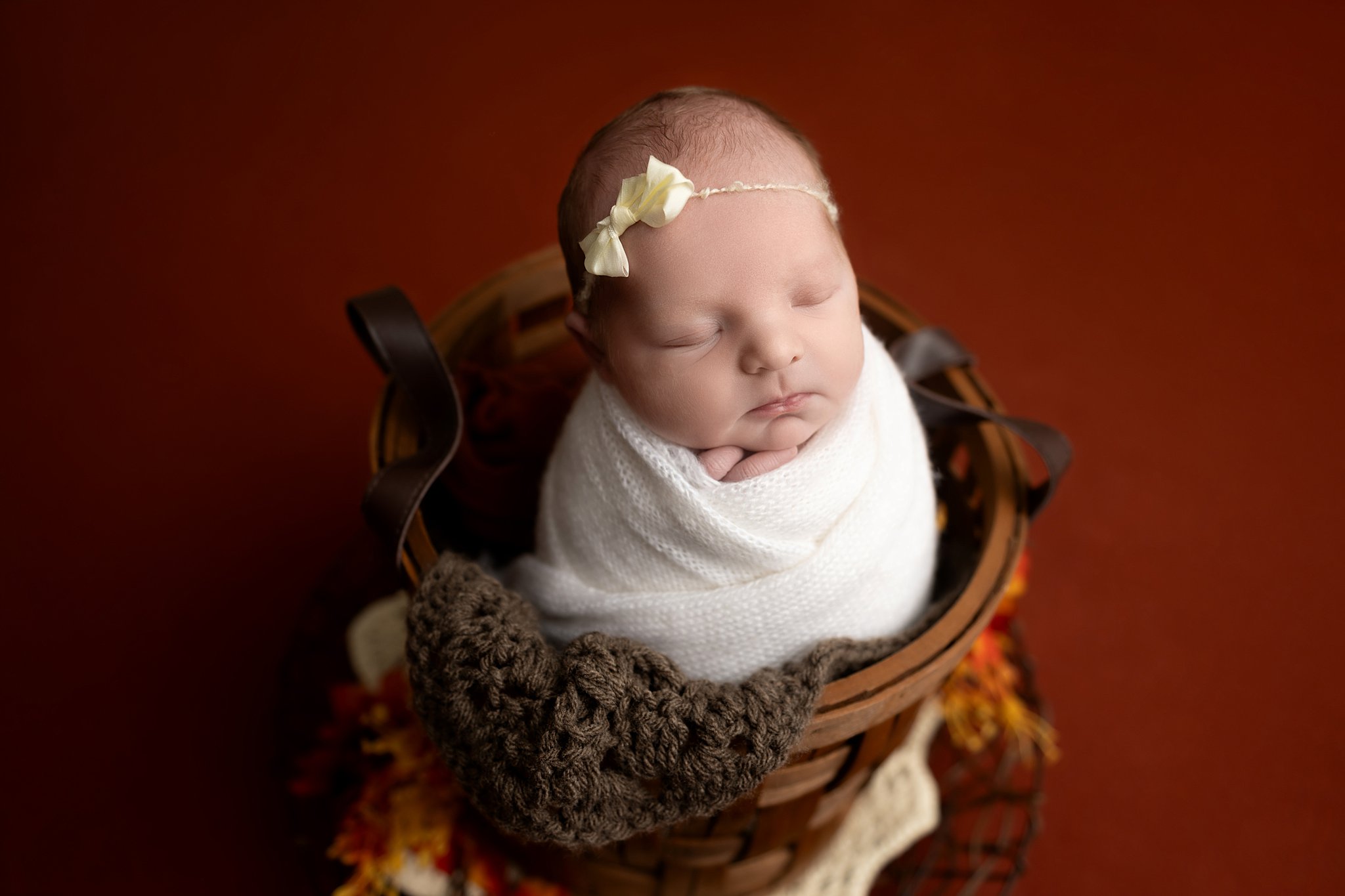 a sleeping newborn baby in a white swaddle sitting up in a wooden basket after visiting wit and whimzy