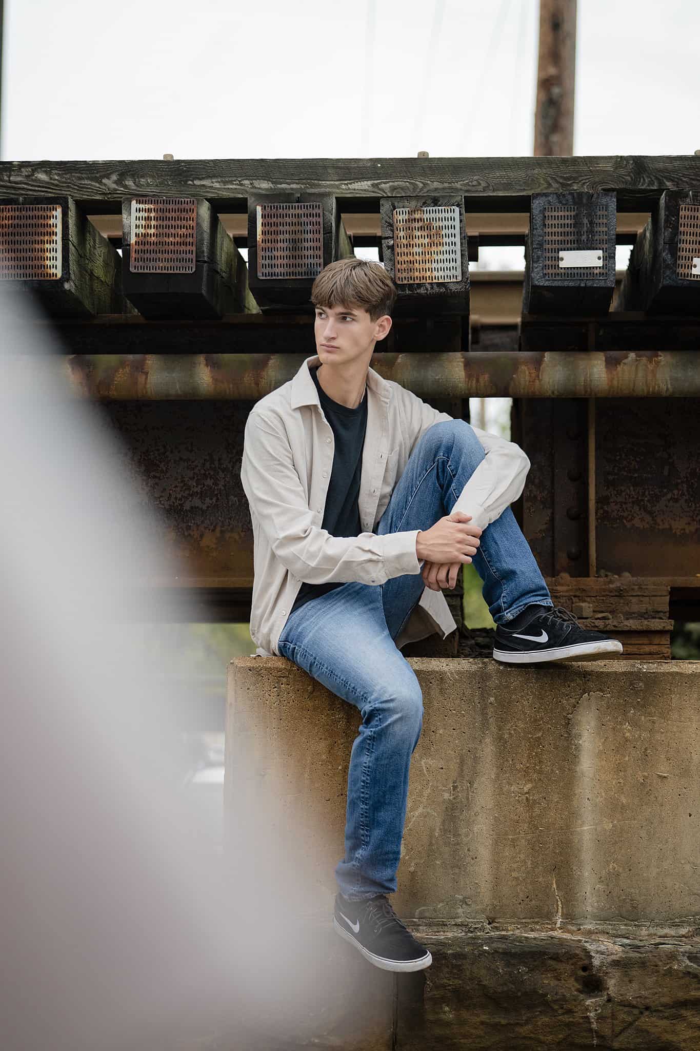 A tall high school senior in jeans sits on the pilling of an old railroad bridge after finding act prep in parkersburg wv