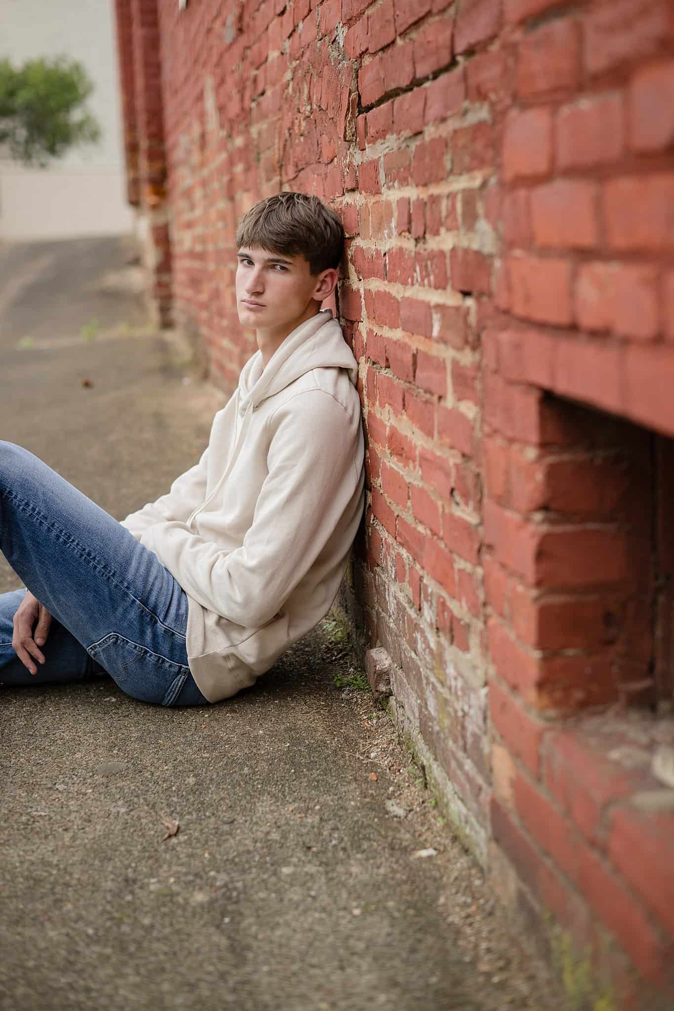 A high school senior sits against a brick wall in a cream hoodie after enjoying act prep in parkersburg wv