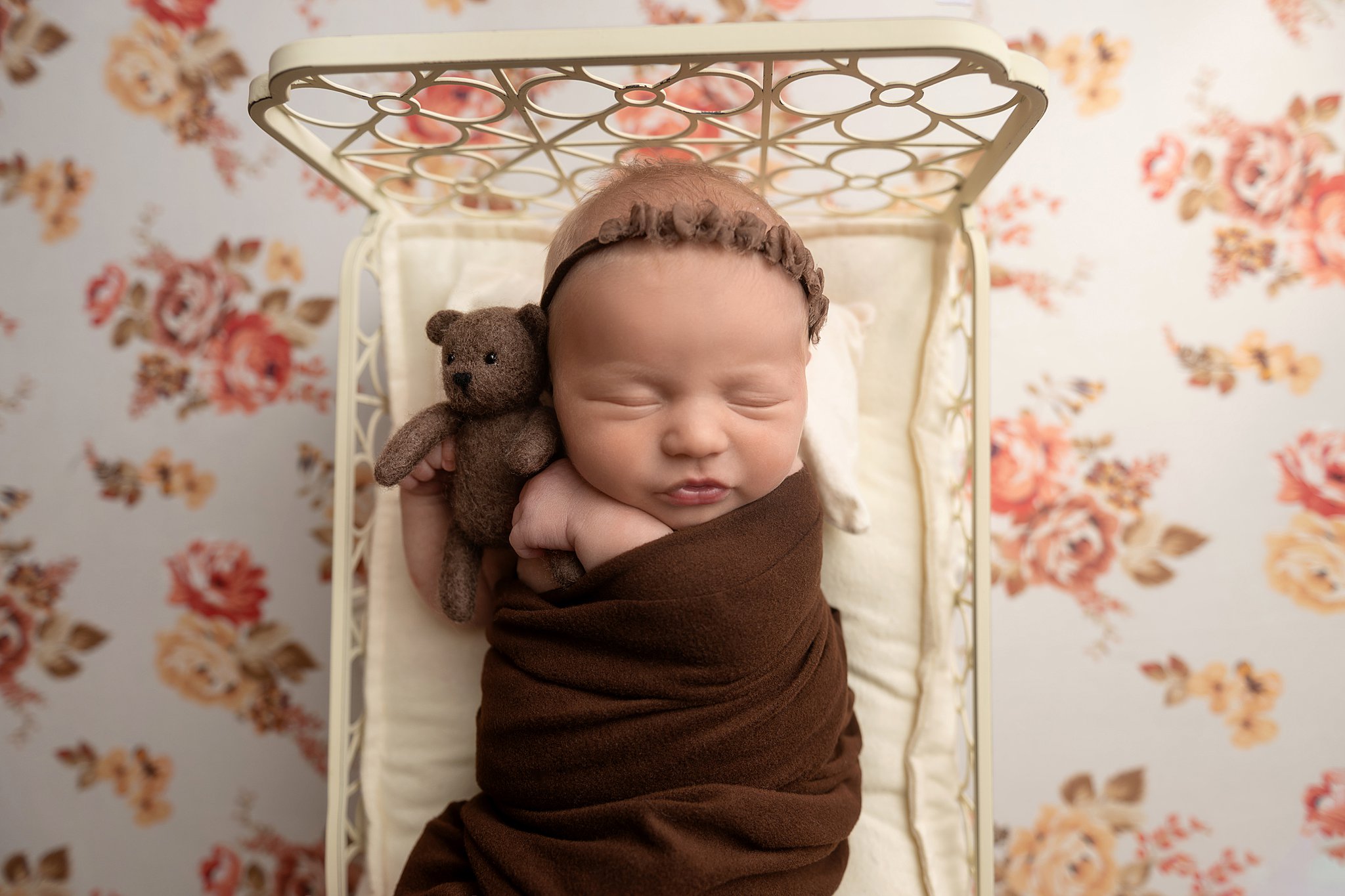 A newborn baby snuggles a brown teddy in a tiny bed while wrapped in a brown swaddle before some baby classes in parkersburg wv