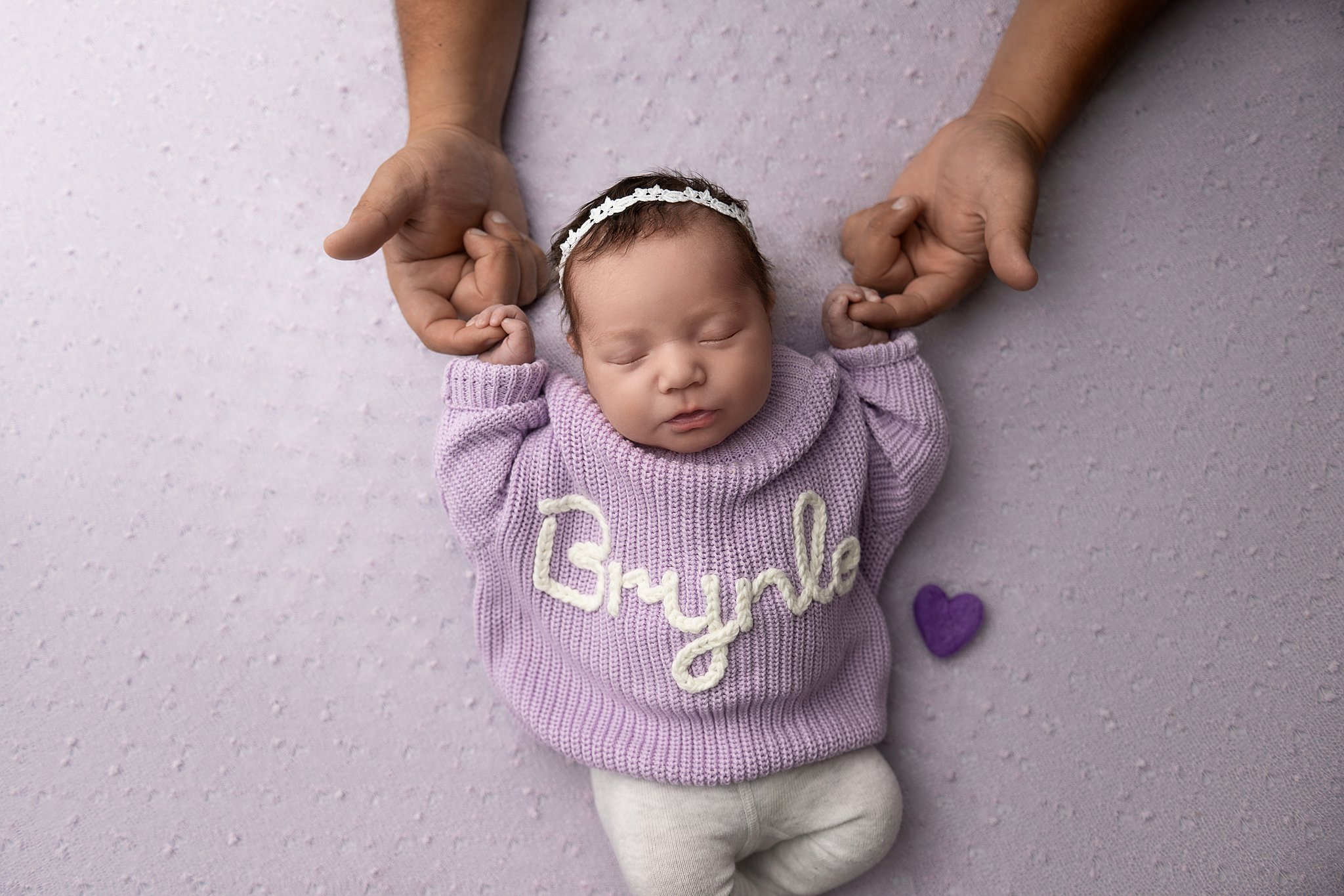 A sleeping newborn girl in a custom knit sweater holds dad's fingers thanks to a postpartum doulas in Parkersburg, WV