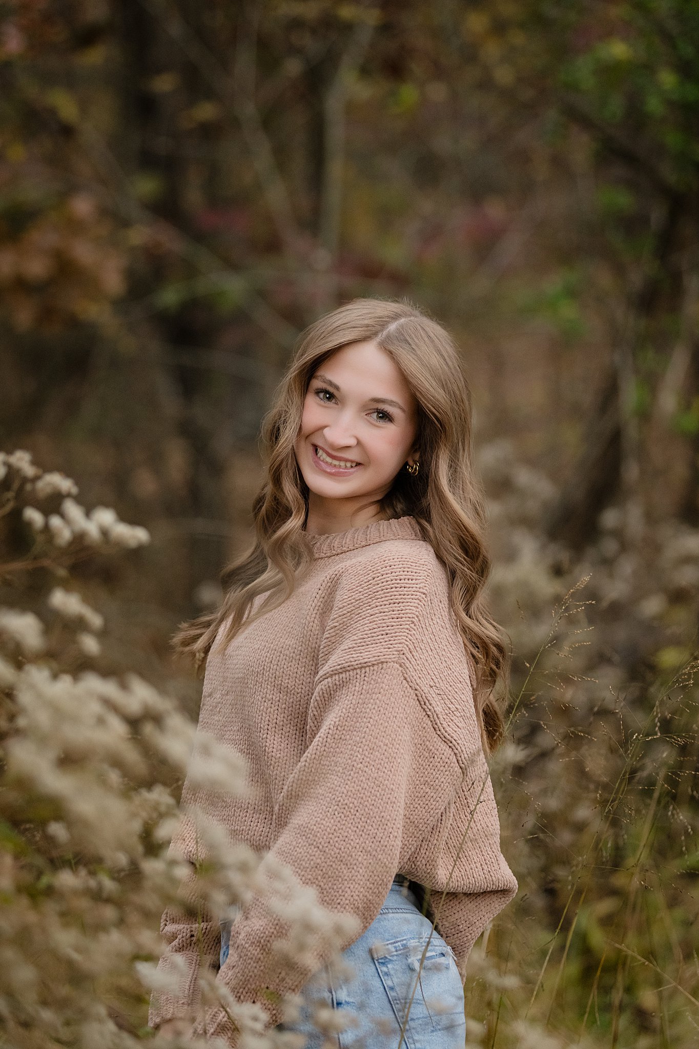 A happy high school senior smiling in a tan sweater in a forest