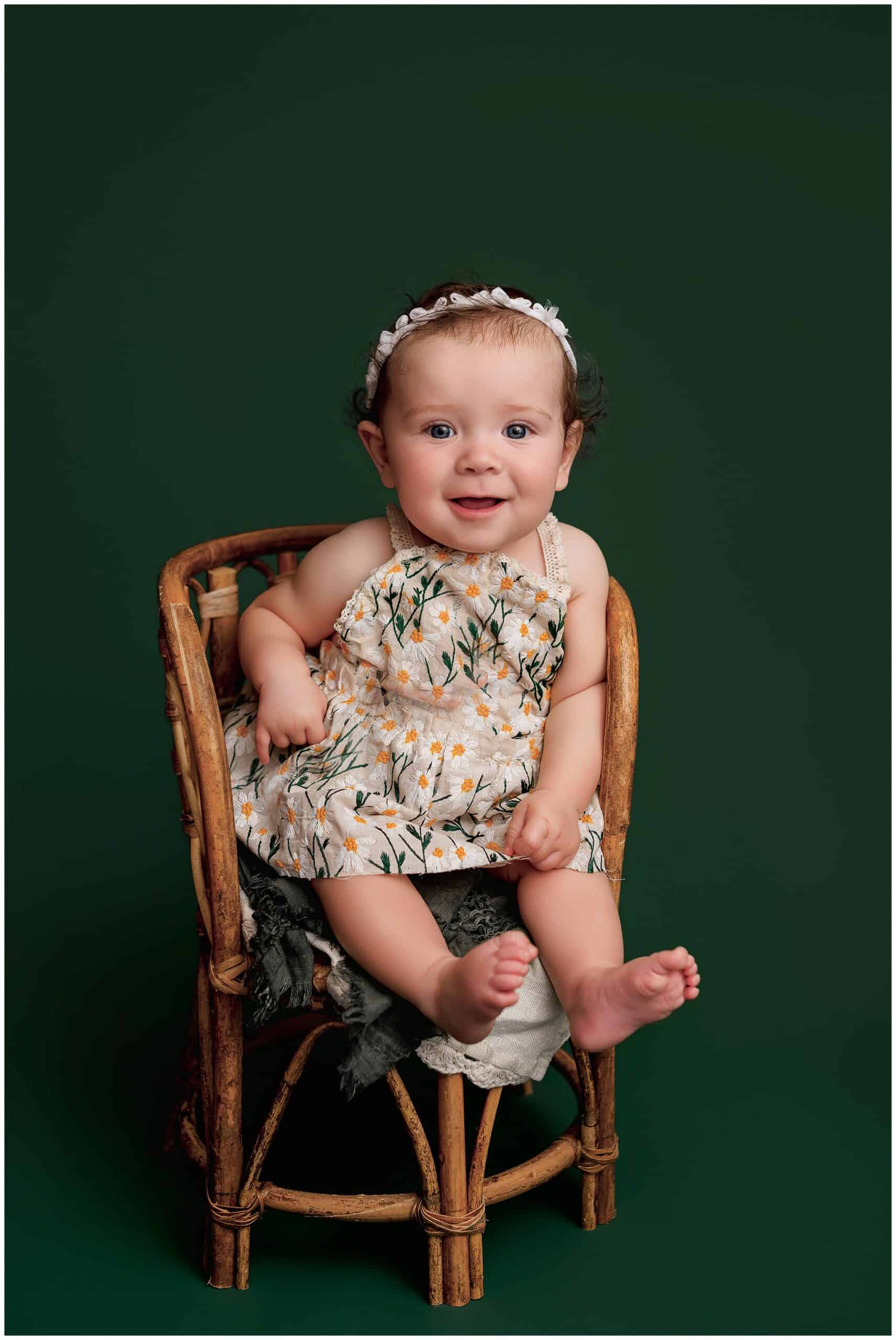 A happy baby girl in a daisy dress sitting in a wicker chair in a studio after mom found Gyms with childcare near Parkersburg, WV
