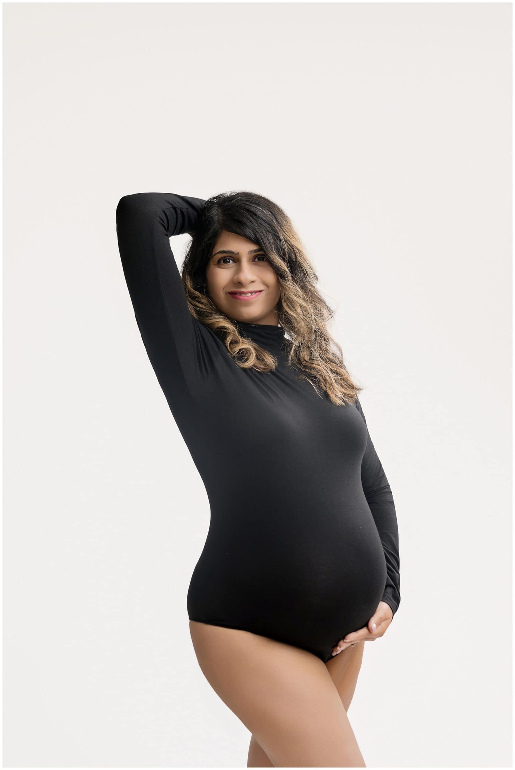 A pregnant woman in a black bodysuit stands with hand under the bump after visiting Petal And Pine Therapy