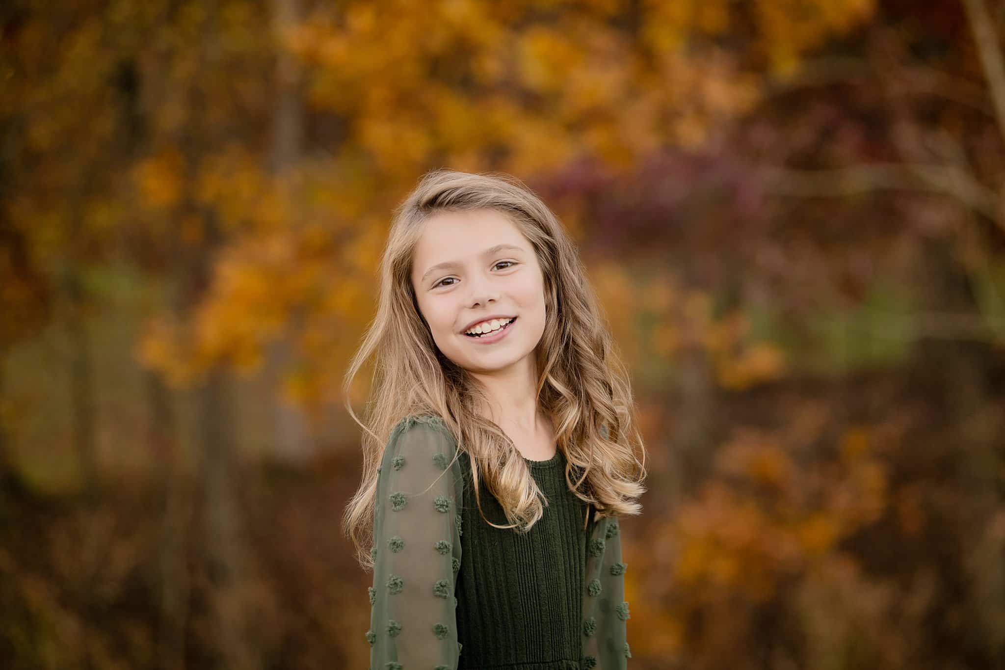 A smiling young girl in a park in fall wearing a green dress after visiting pumpkin patches near parkersburg, WV